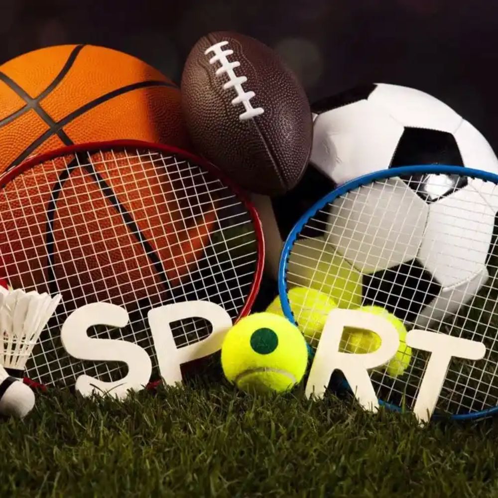 Collection of sports equipment including a basketball, football, tennis balls, and badminton racket on grass with 'SPORT' spelled out.
